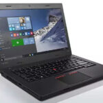 Open Lenovo ThinkPad laptop showing Windows desktop with mountain wallpaper, keyboard, and red TrackPoint in the center of the keyboard.